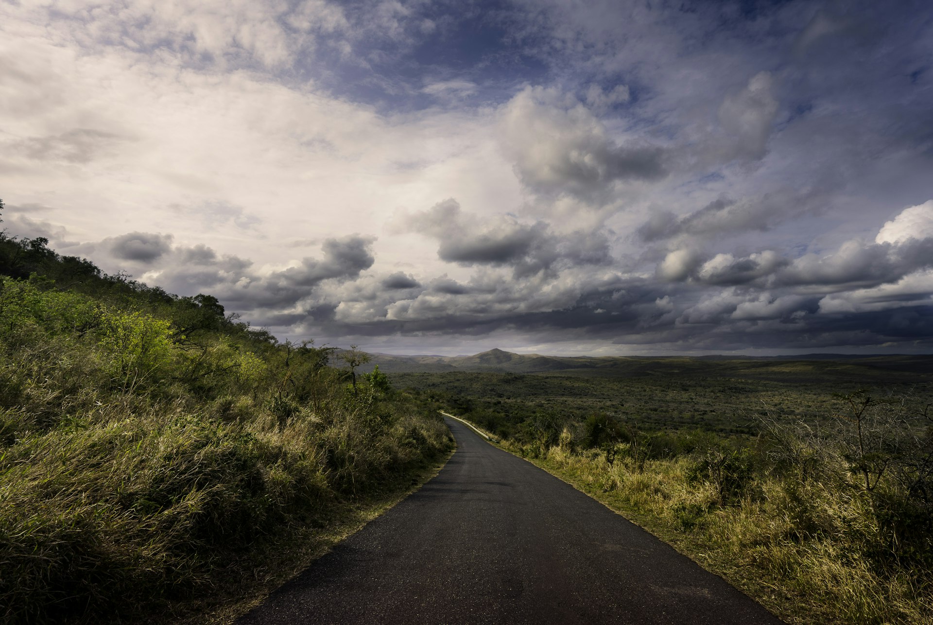a road going down a hill under a cloudy sky