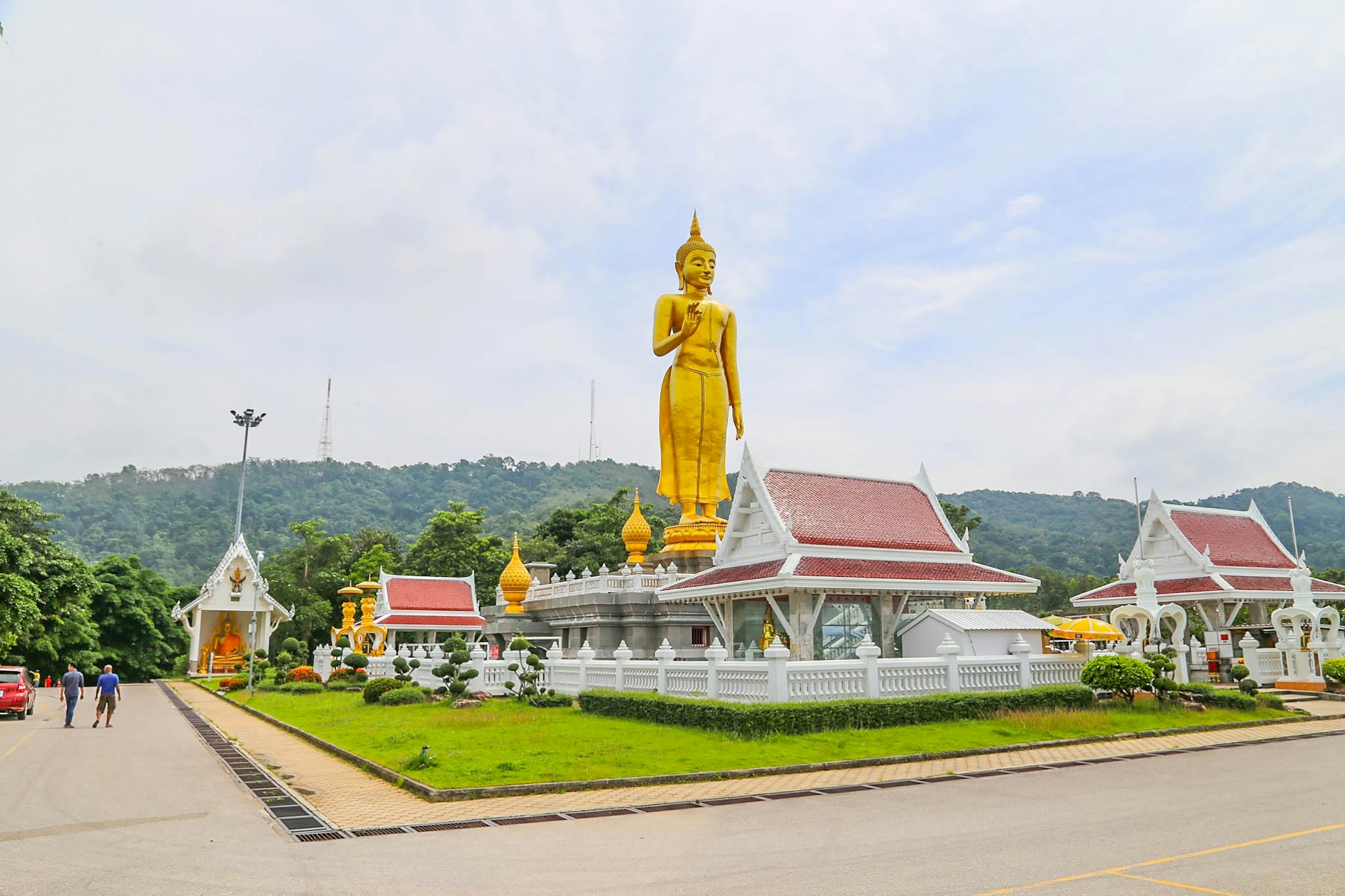 a large golden buddha statue sitting in the middle of a lush green field
