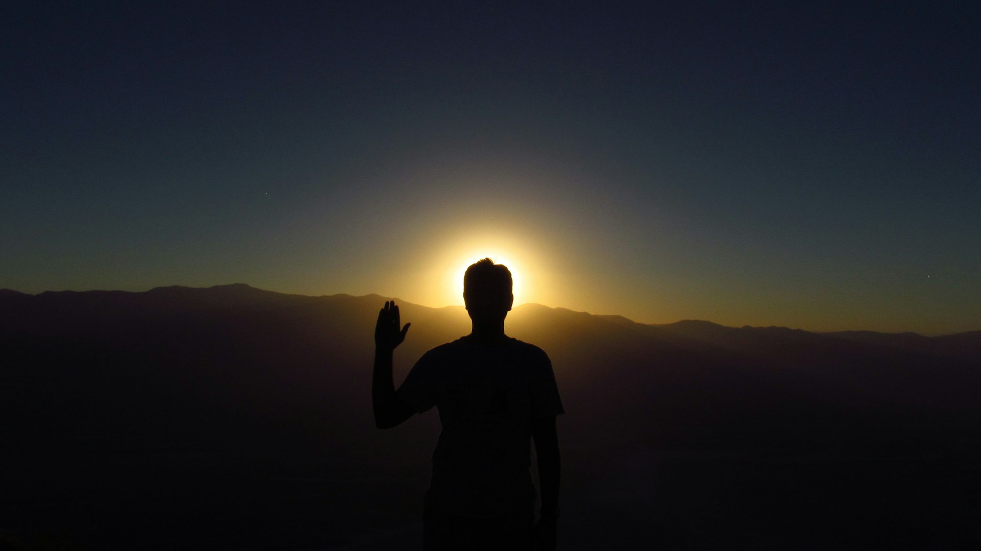 a silhouette of a man holding a cell phone in front of the sun