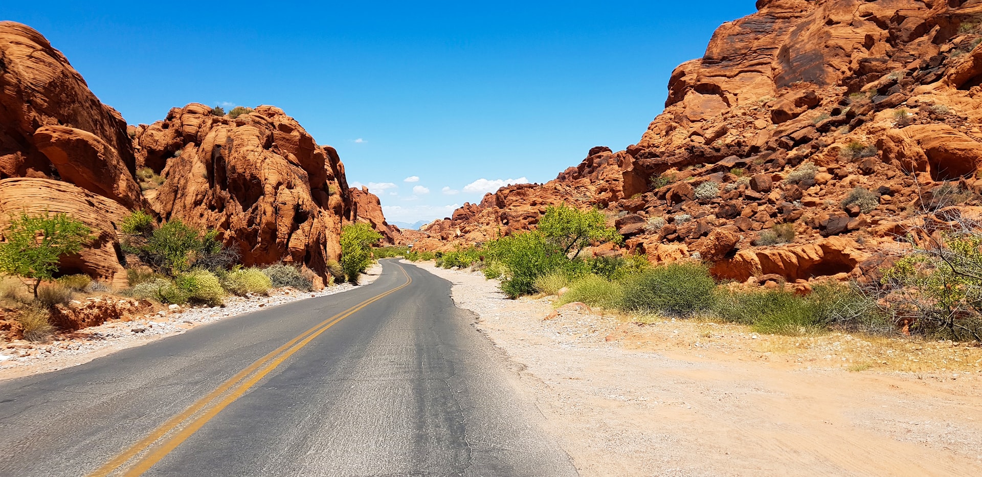 gray asphalt road between brown rock formation under blue sky during daytime