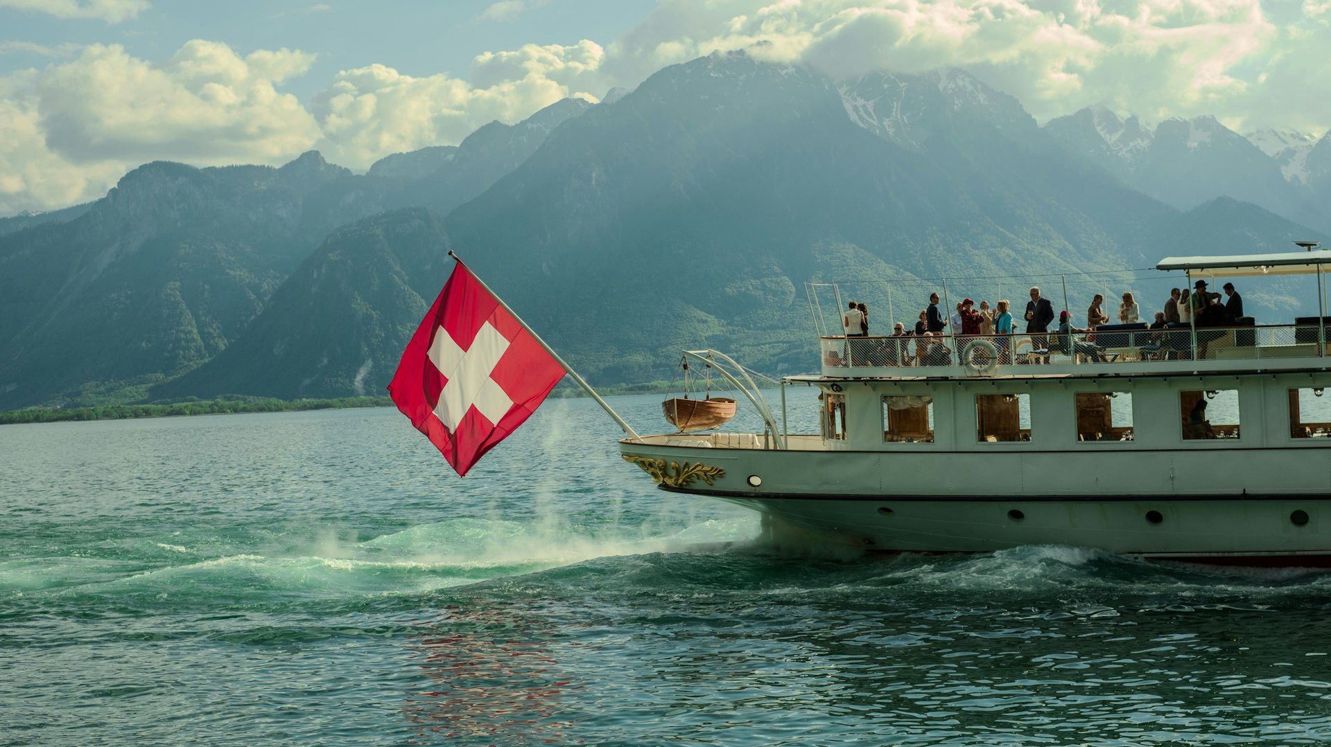 A swiss boat cruises on a lake near mountains.